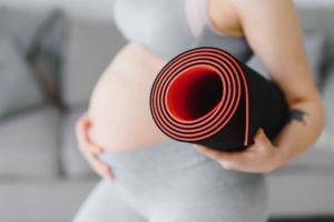 Smiling pregnant woman in sportswear ready for morning gymnastics or exercise. Happy young female follow healthy lifestyle during pregnancy, hold yoga mat for Pilates or stretching.
