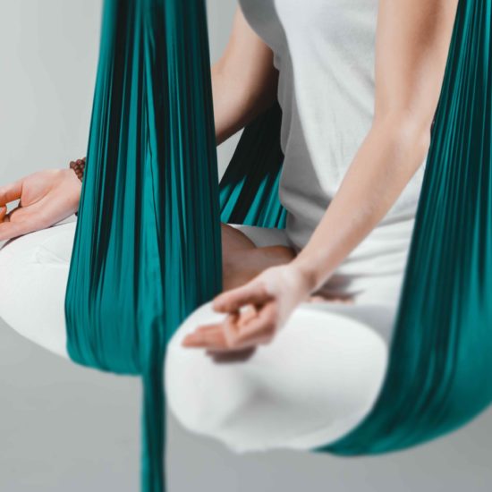 An adult woman practices different inversion - anti-gravity yoga positions in a bright well lit studio.